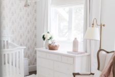 a chic neutral nursery with a bead chandelier, a vintage chair and crib, a dresser, white rugs and a Moroccan pouf