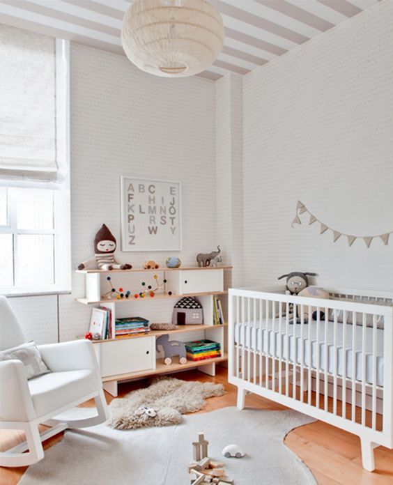 a neutral modern nursery with a rocker chair, a crib, a creative sideboard, rugs and striped walls and a ceiling