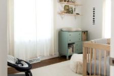 a welcoming neutral nursery with a green changing table, wicker and wooden touches, a neutral rug and a sheer curtain