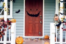 a whimsical Halloween porch with carved pumpkins on steps, candle lanterns, paper bats, fall leaves and a grin door