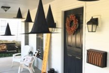 witch hats suspended, natural pumpkins, candle lanterns and a bold fall bloom wreath for a Halloween porch