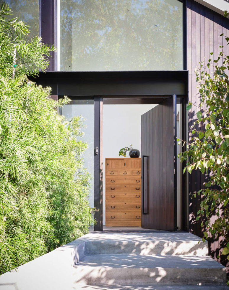 The front door is clad with dark wood and it's pivoting, which gives a modern feel to the space
