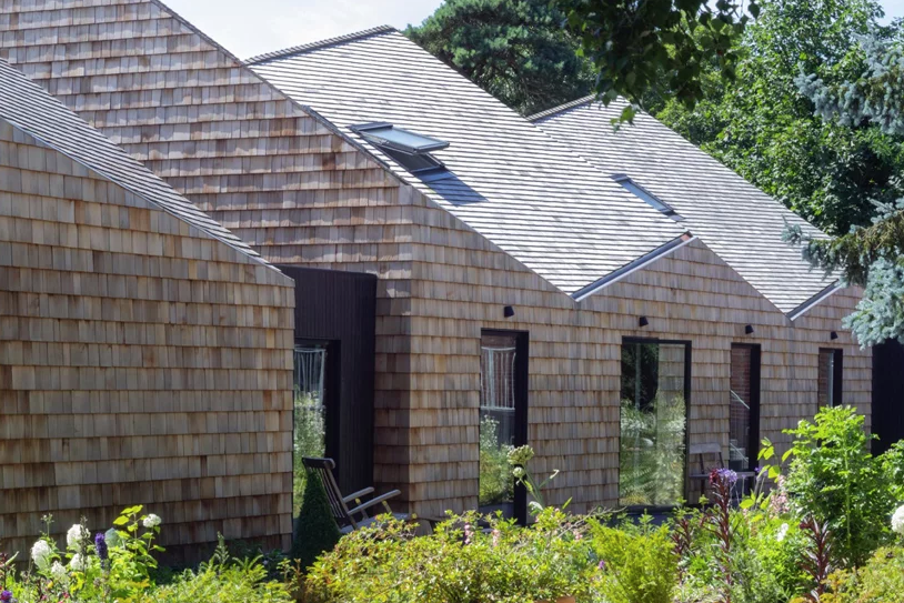 The house is fully clad with shingles and it looks like a fresh take on a traditional barn, with sculptural shapes