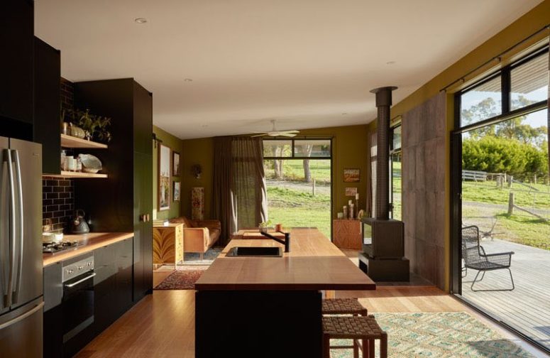 The kitchen and living room are united into one space, with a hearth, a large kitchen island with an eating space and dark kitchen furniture The kitchen and living room are united into one space, with a hearth, a large kitchen island with an eating space and dark kitchen furniture