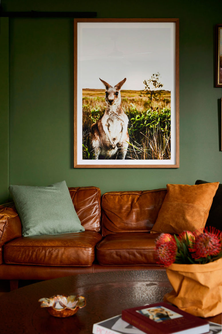 The living room is done with green walls, a brown leather sofa, a rich toned wooden table and a bold artwork The living room is done with green walls, a brown leather sofa, a rich-toned wooden table and a bold artwork