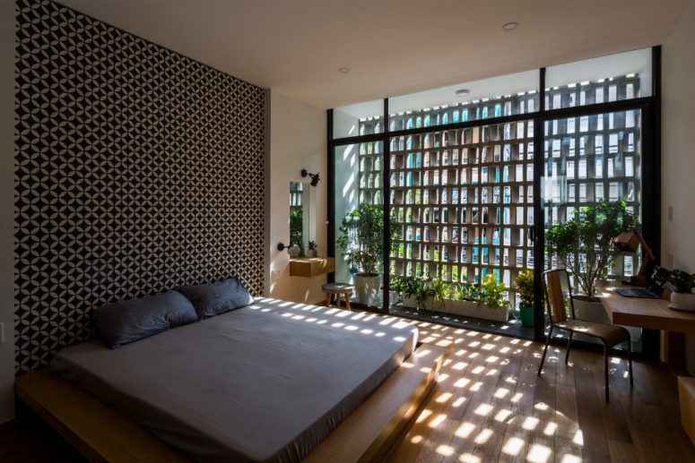 The bedroom features a printed wall, a platform bed and shades on the window plus much greenery