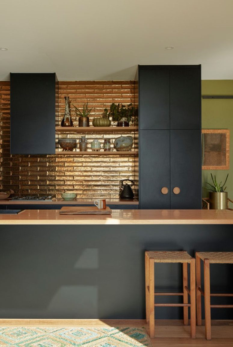 The kitchen features a shiny metallic backsplash and wooden handles to create a contrast with dark furniture The kitchen features a shiny metallic backsplash and wooden handles to create a contrast with dark furniture