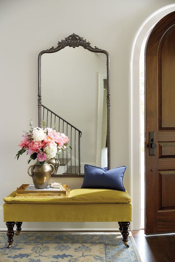 a large vintage mirror in a silver frame and a mustard velvet bench make up a gorgeous entry