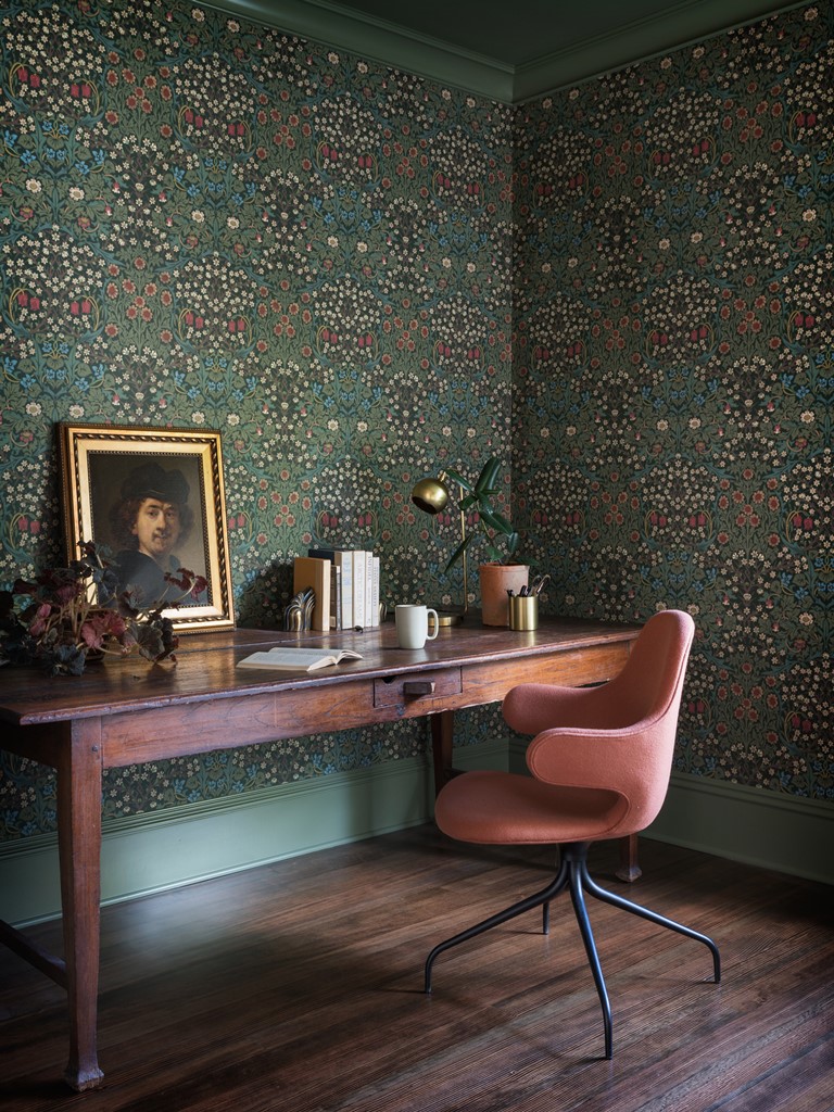 The home office is done with a large vintage desk, a pink chair and moody printed wallpaper
