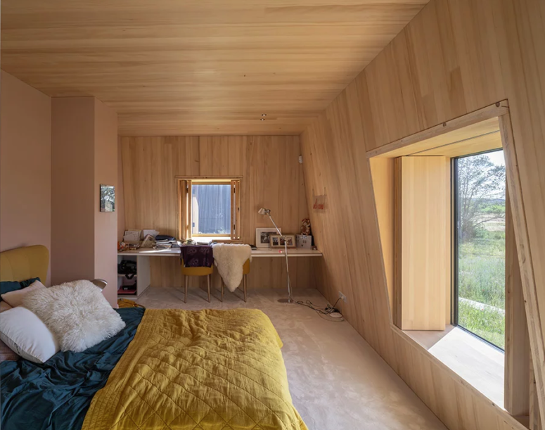 a tiny home office in a bedroom is a working solution for many homes This bedroom is done with plywood completely, there are large windows, a mini home office in the corner and a large bed