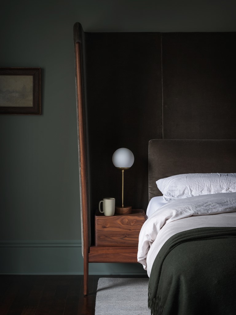 The bedroom is dark and welcoming, with an upholstered bed and an oversized headboard