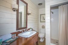 08 The bathroom is done with white shiplap and tiles, a walk-in shower and a vanity of rich stained wood