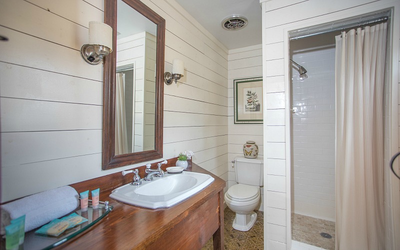 The bathroom is done with white shiplap and tiles, a walk in shower and a vanity of rich stained wood