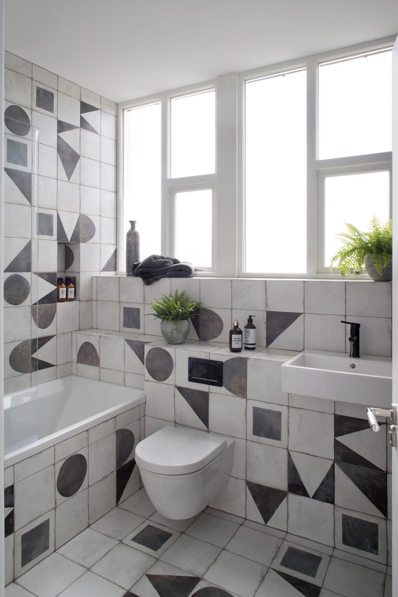 This is a black and white bathroom with geometric tiles and a bathtub, there's a window with frosted glass