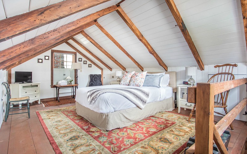 The bedroom is done with wooden beams, white shiplap, printed rugs and elegant neutral furniture
