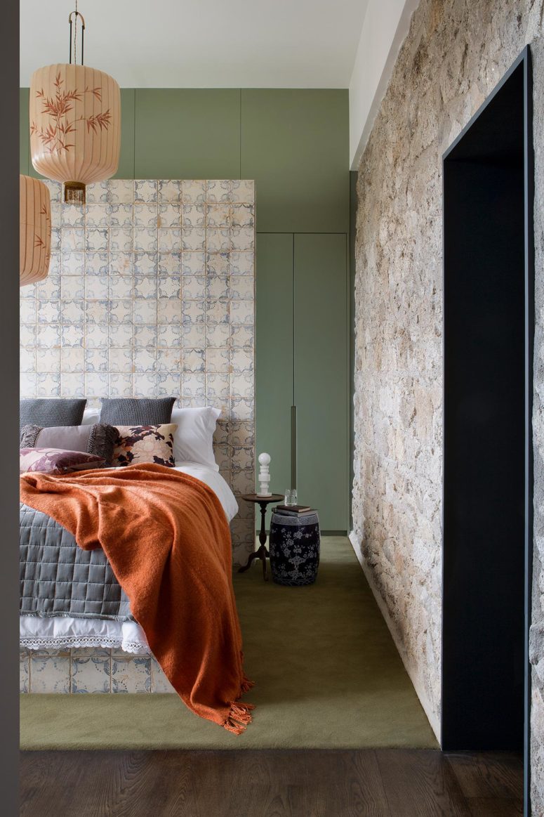The master bedroom is done with a tile covered bed, a stone wall, a green storage unit and bright bedding The master bedroom is done with a tile covered bed, a stone wall, a green storage unit and bright bedding