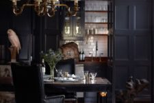 09 a chic dark kitchen with paneled cabinets, a white tile backsplash and an elegant chandelier and furniture