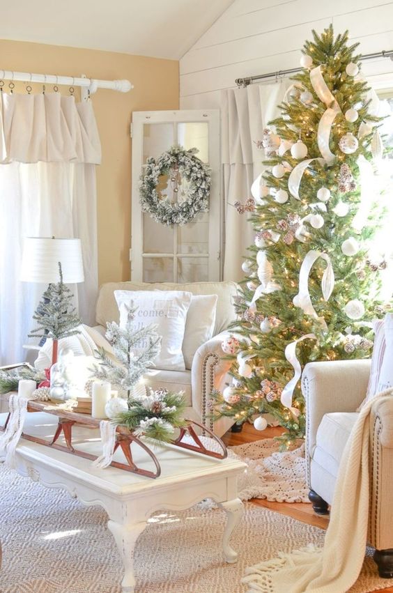 a sleigh with candles, pinecones, snowy evergreens, a snowy wreath with bells and a Christmas tree with white balls, pinecones and ribbons