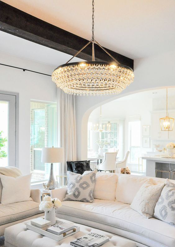 a neutral living room with dark wooden beams and a large and chic crystal chandelier