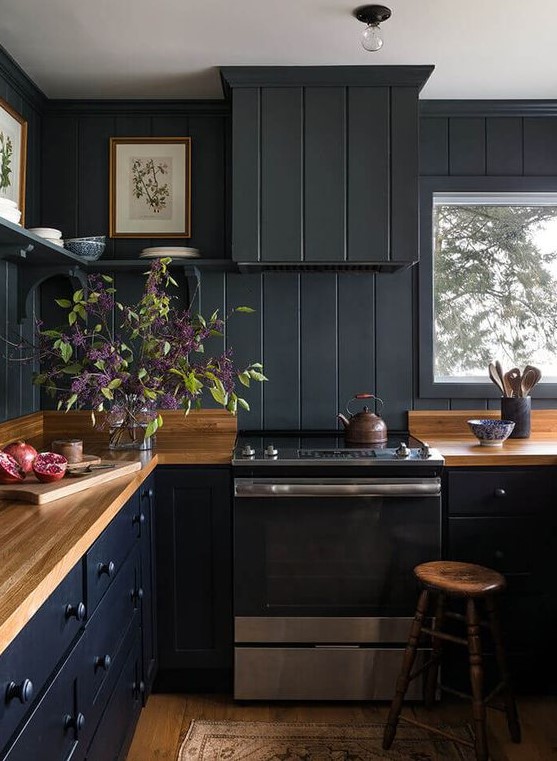 a black farmhouse kitchen done with beadboard, light-colored wooden countertops and stools plus open shelving