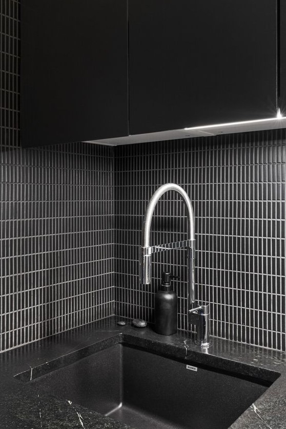 a black minimalist backsplash with narrow tiles placed vertically and highlighted with white grout