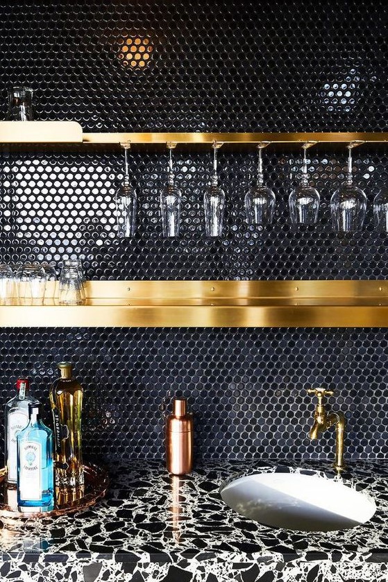 a black penny tile backsplash and gold shelves and fixtures make up a very chic and refined combo