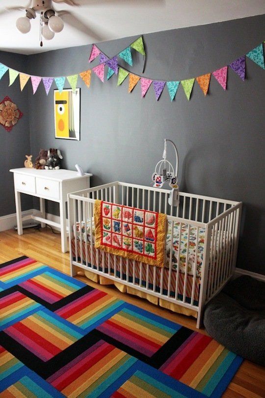 a bold nursery with grey walls but striped rugs, colorful buntings, colorful bedding and artworks for fun