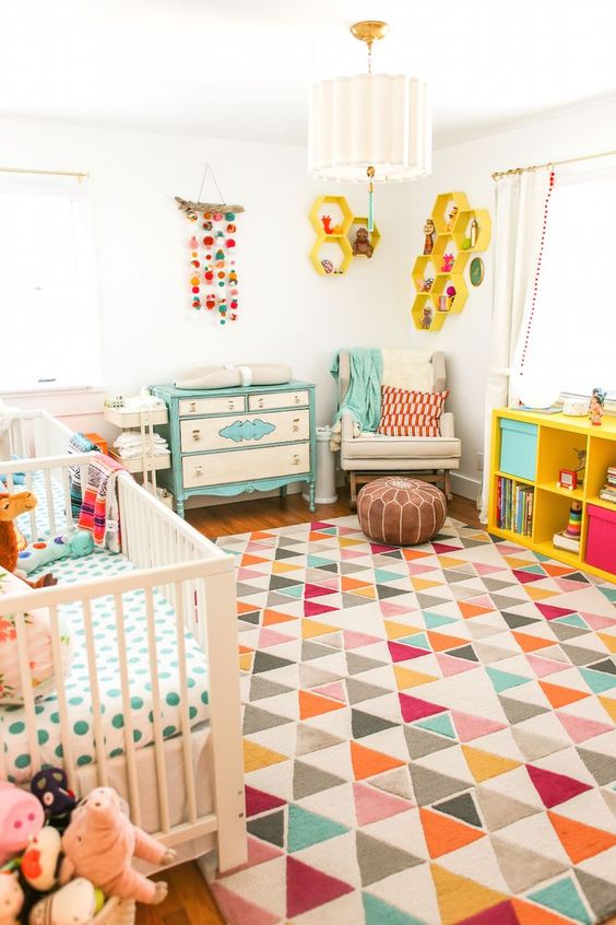 a bright mid-century modern nursery with a geometric rug, colorful bedding, a mobile, a bright changing table and yellow shelves
