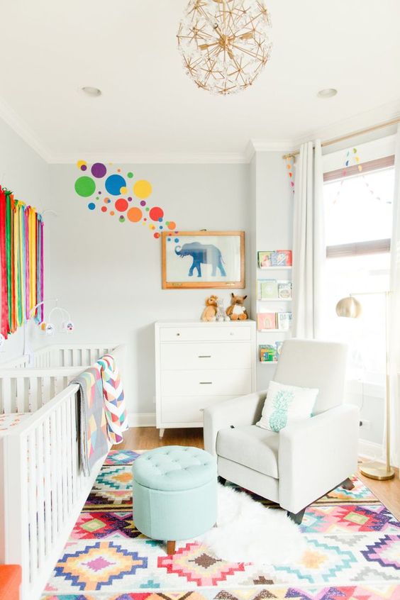 a bright modern nursery with a printed rug, a rainbow hanging, colorful bubbles and bright bedding