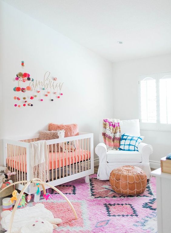 a bright nursery with a printed rug, colorful bedding and pillows, pompom garlands and fun and colorful toys