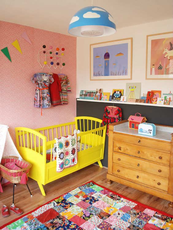 a bright nursery with a yellow bed, a quilted rug, colorful artworks and colorful books on the ledges