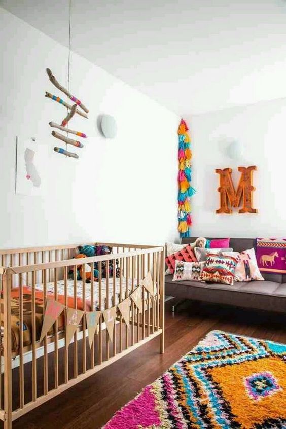 a colorful boho nursery with a bright rug, colorful tassel garlands, a mobile and bright textiles all over