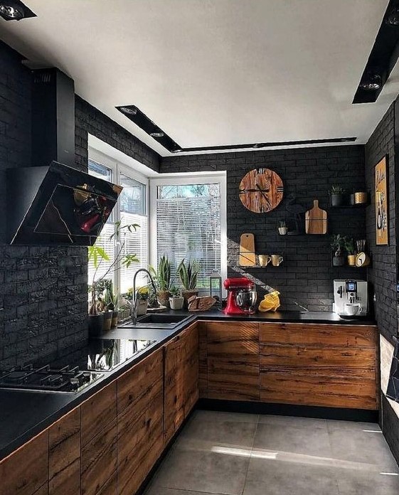 a contemporary black kitchen with black brick walls, light-colored wood cabinets, black countertops and a hood
