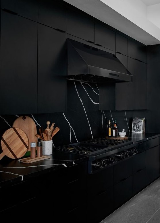 a dramatic black kitchen with black marble countertops and a backsplash, with a black hood and appliances is very elegant
