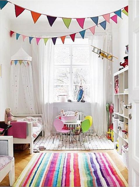 a fun nursery with colorful buntings, a bright striped rug and bedding plus colorful chairs by the table