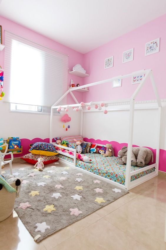 a fun nursery with pink walls, colorful bedding and a fun rug, colorful toys and artworks is amazing space