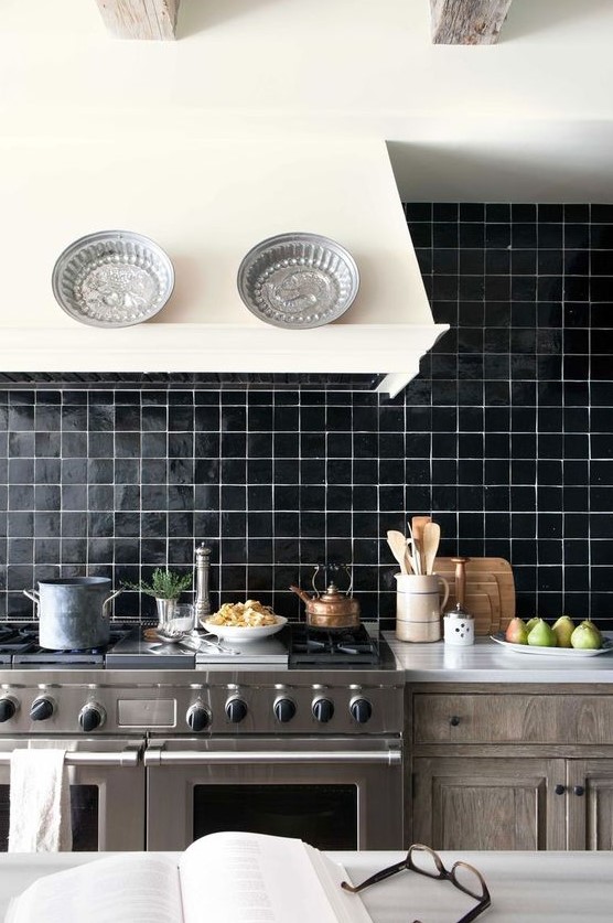 a stained wooden kitchen, a creamy hood, a black glossy tile backsplash and stainless steel appliances is bold and cozy