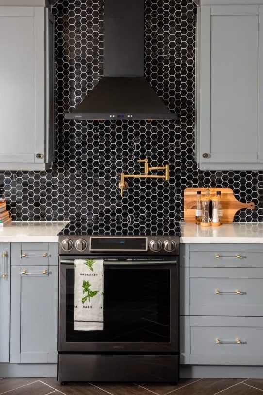a stylish grey farmhouse kitchen with white countertops and a black hex tile backsplash plus a black hood looks very refined