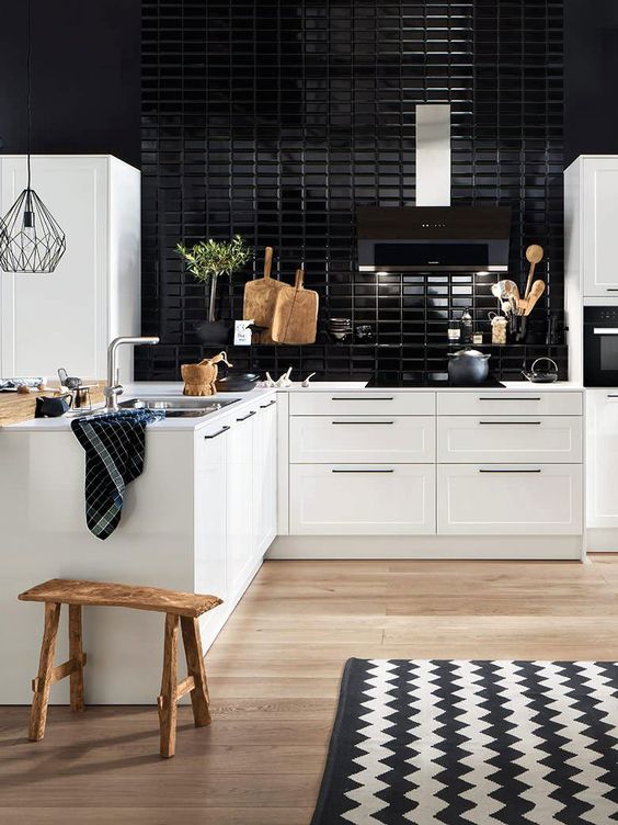 a stylish modern white kitchen of an L-shape, with a glossy black tile backsplash and a wooden stool, some greenery and a chevron rug