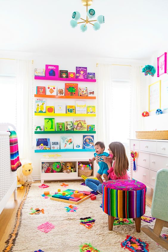 a super colorful nursery with rainbow shelves, a bright rug, bedding and colorful toys