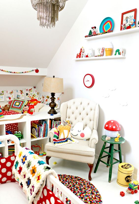 a tiny but super colorful nursery with bright bedidng, a colorful pompom rug, lots of bright toys, books and various accessories