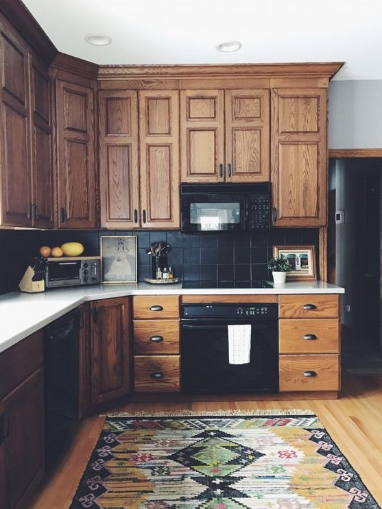 a vintage rustic kitchen with stained cabinetry, a black tile backsplash and white countertops plus a bold boho rug