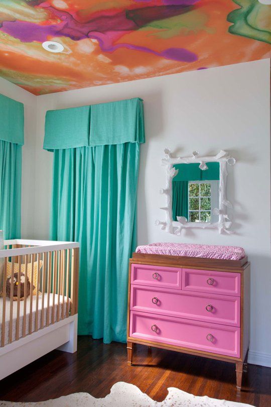 a whimsical nursery with turquoise curtains, a pink dresser, colorful watercolor ceiling and fun bedding