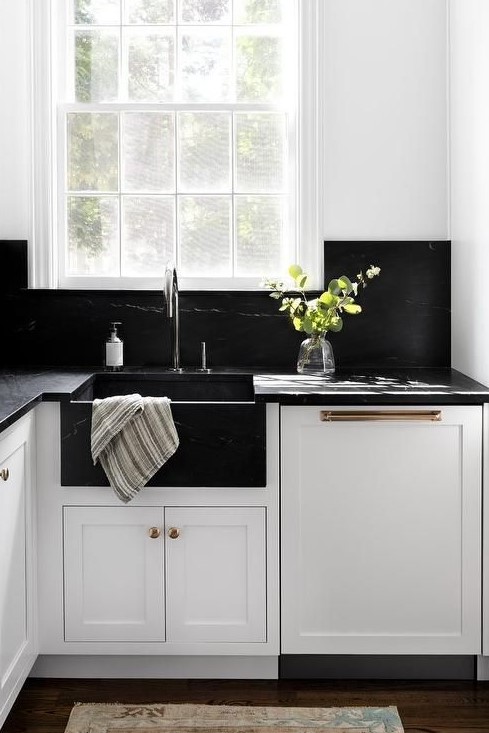 a white farmhouse kitchen with black quartz countertops and a matching backsplash plus mismatching metals for fxitures