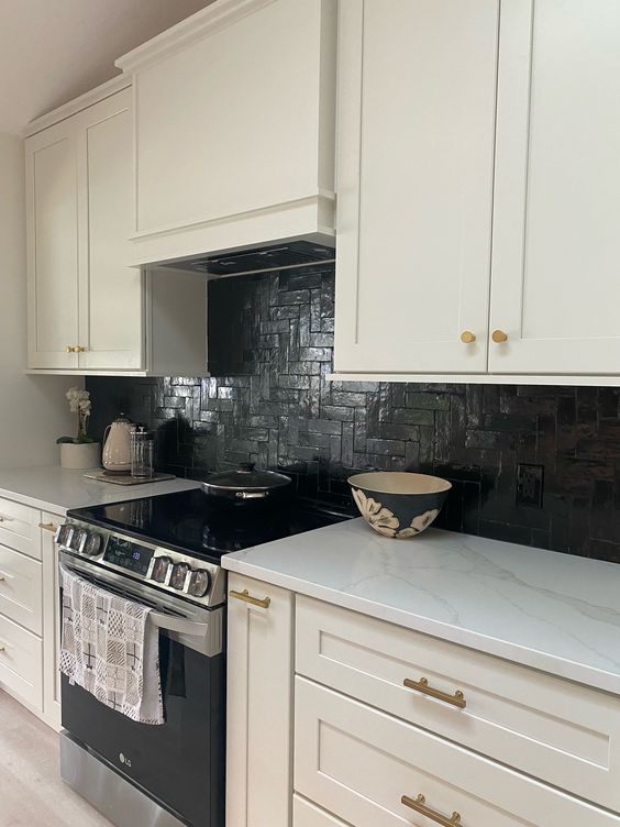 a white farmhouse kitchen with shaker style cabinets, a black herringbone tile backsplash and white stone countertops