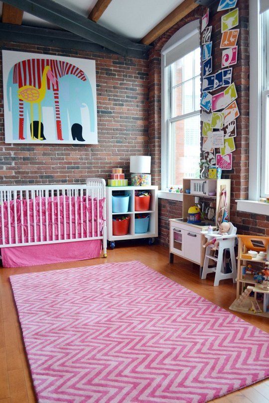 pink bedding, a pink rug, colorful artworks make this nursery with brick walls very whimsy and very bold