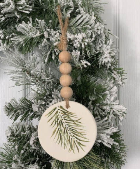 a rustic Christmas ornament of a wood slice with painted evergreens, wooden beads and twine is very fun and cool