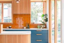 04 a warm-colored and wood slab clad kitchen with some classic blue cabinets with wooden handles