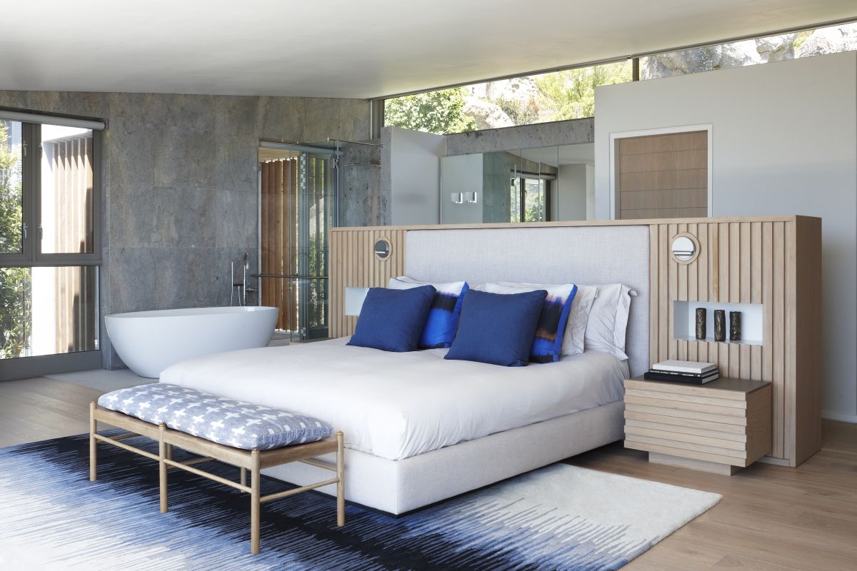 The master bedroom features a bathtub, there's a bright rug and a bed with blue pillows