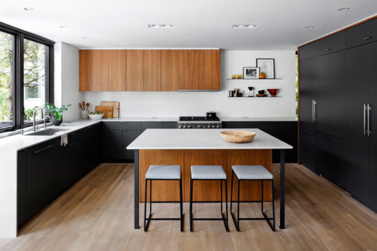 The kitchen is done with black and stained wooden cabinets, there's a kitchen island and some stools The kitchen is done with black and stained wooden cabinets, there's a kitchen island and some stools
